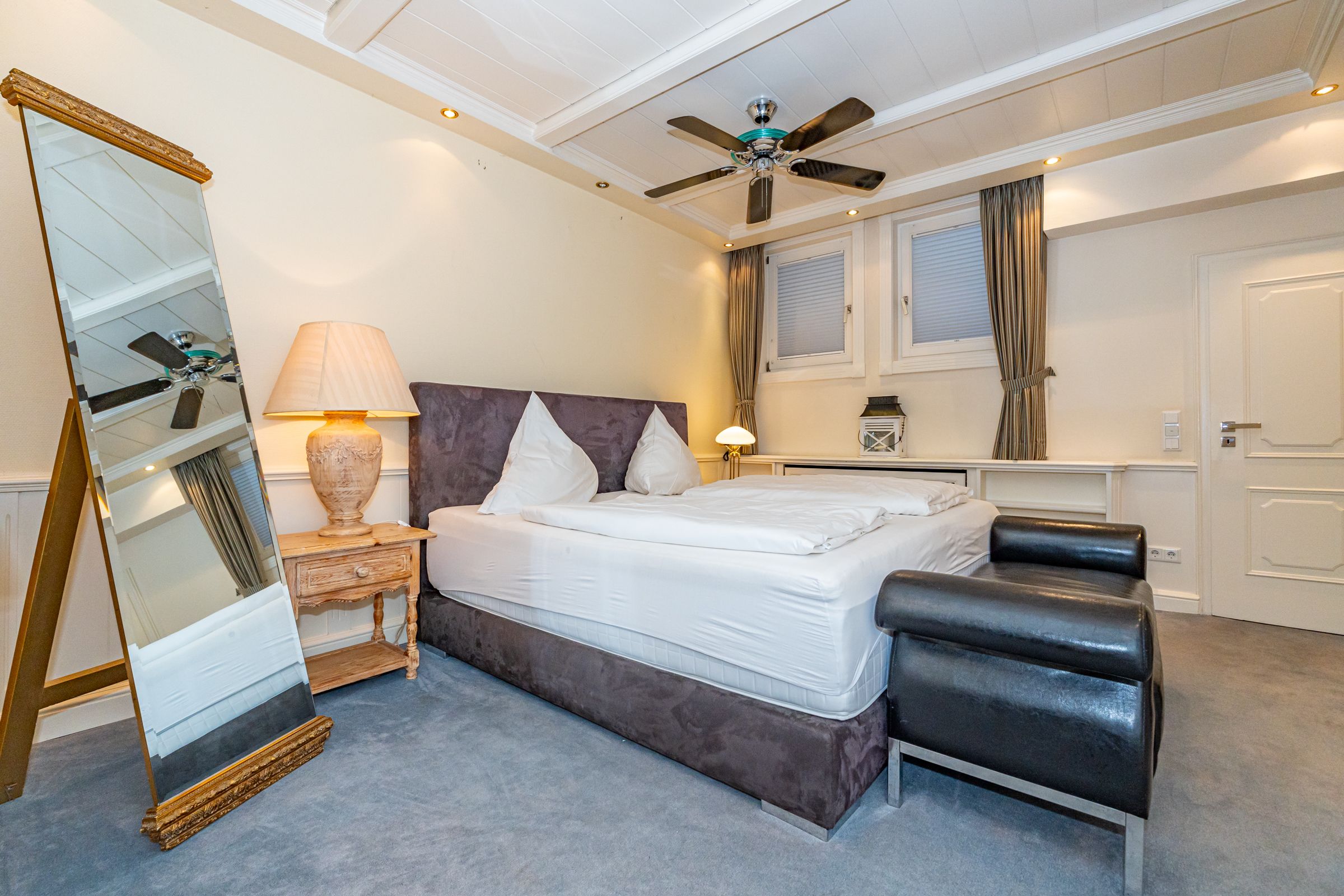 Doppelbett, Teppichboden, Deckenventilator, Schwarzes Sofa und Spiegel
