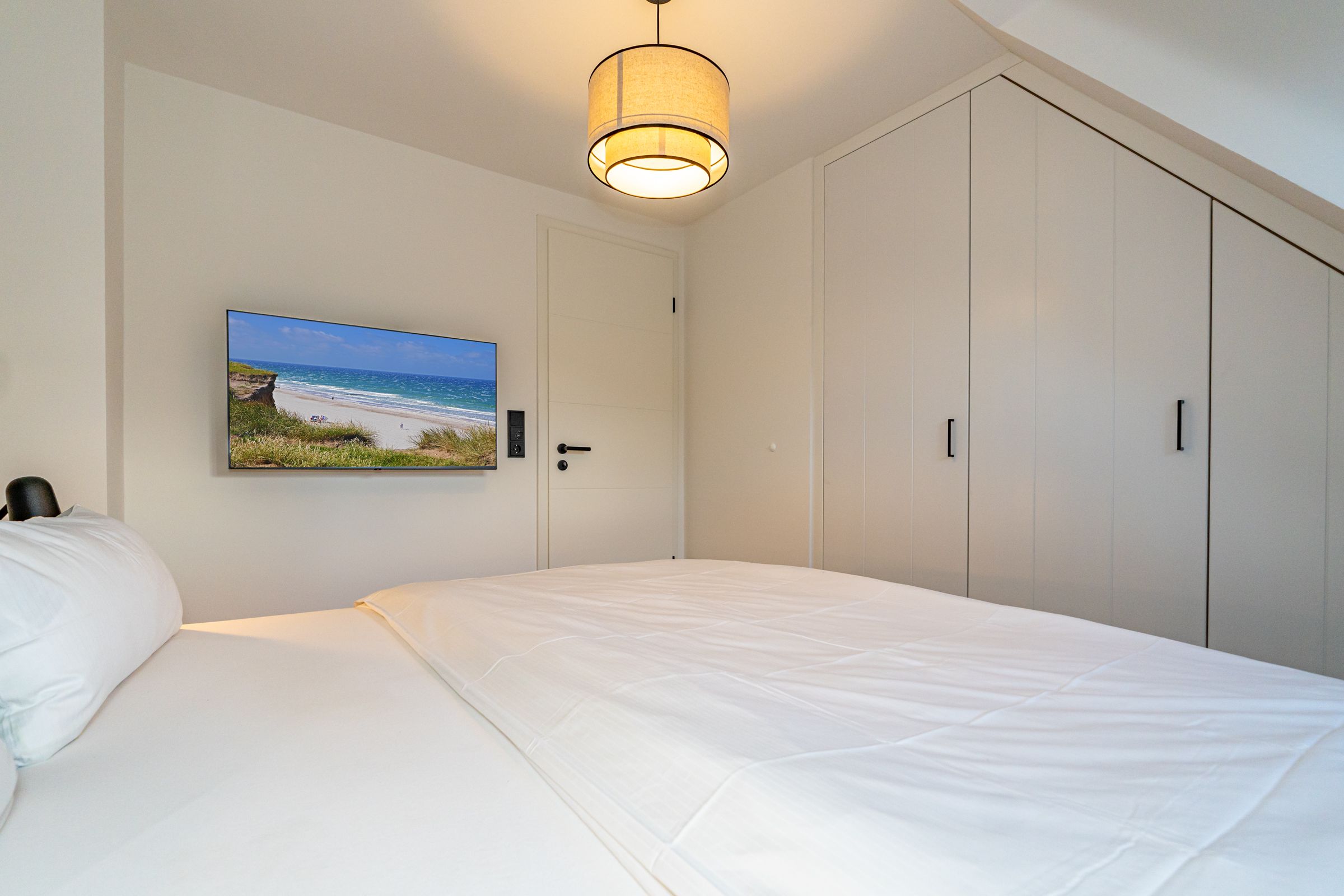 Schlafzimmer mit Doppelbett, Einbauschrank und Tv an der Wand neben der Zimmertür