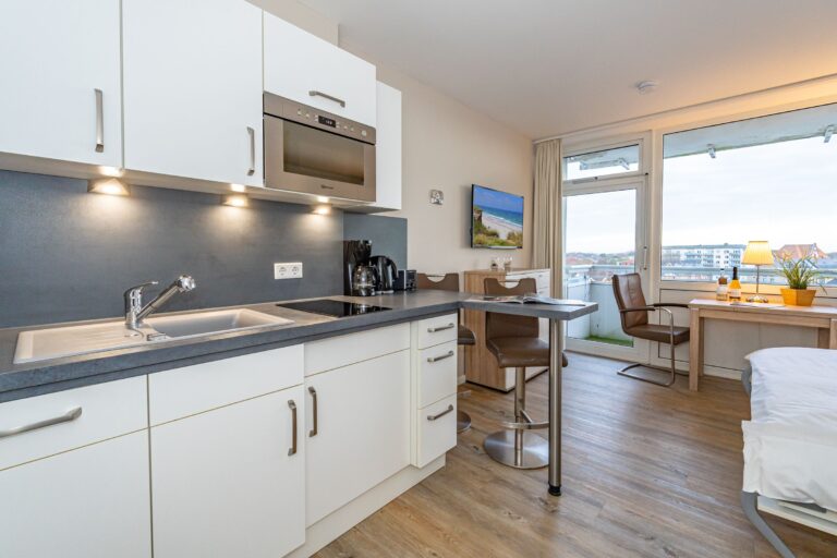 Küchenzeile mit Herd und Mikrowelle. rechts: kleiner Essbereich. Im Hintergrund: Blick auf Westerland