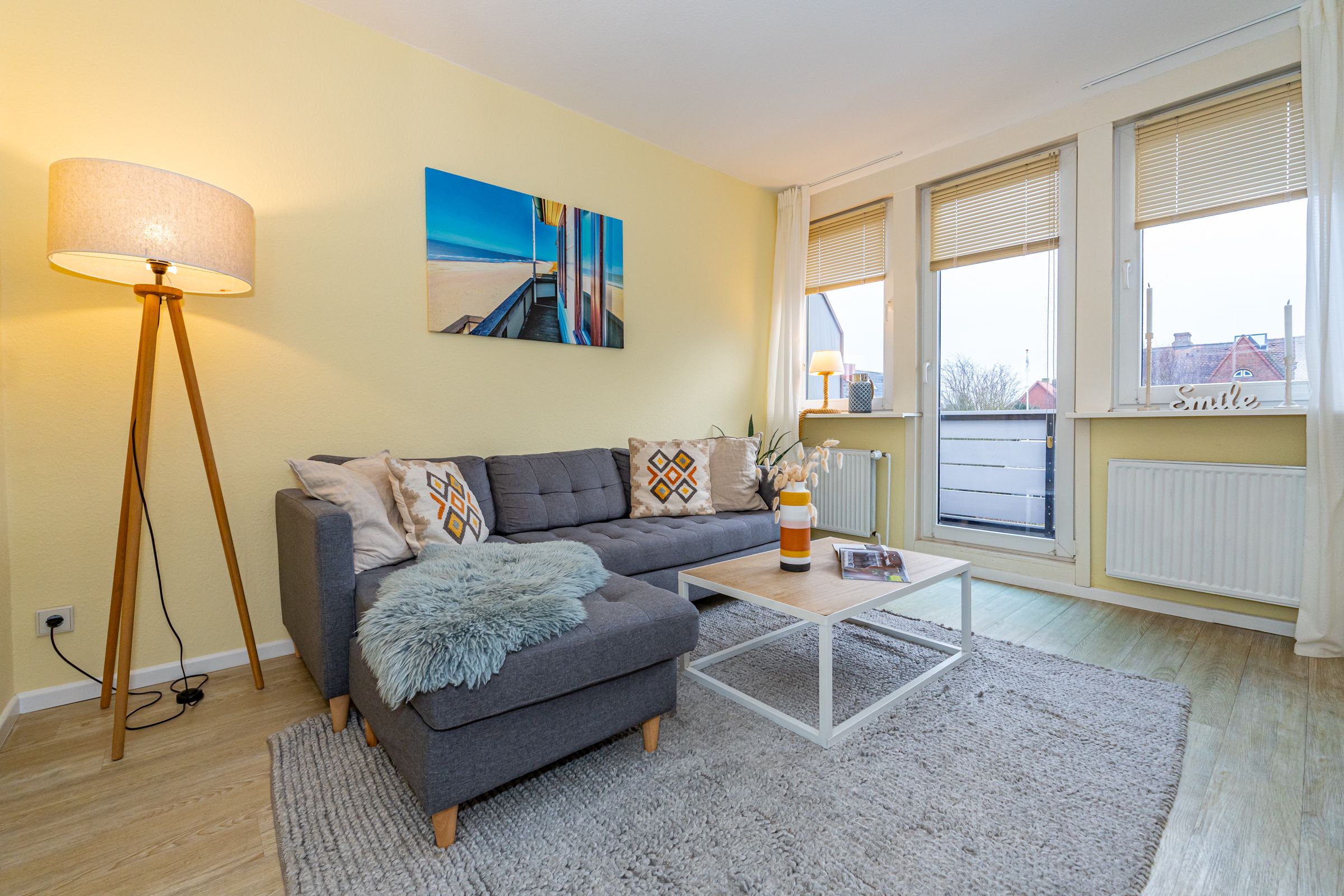 Sofa und Wohnzimmertisch mit Dekorationsartikeln und Blick auf die Balkontür und Fenster.