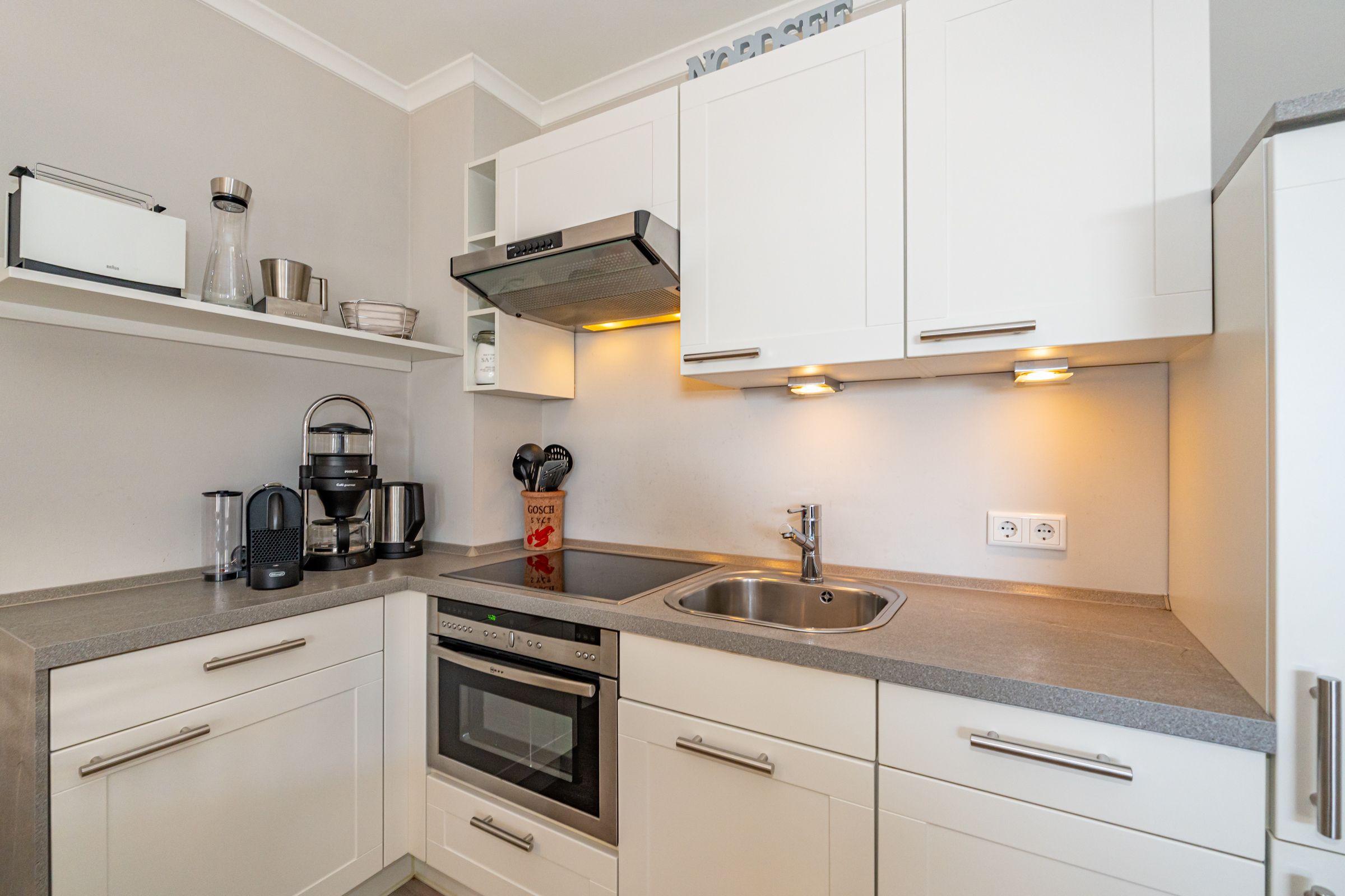 kleine Küche mit Hängeschrank und Arbeitsfläche über Eck. Ausstattung: Kaffeemaschine, Toaster, Herd und Ofen
