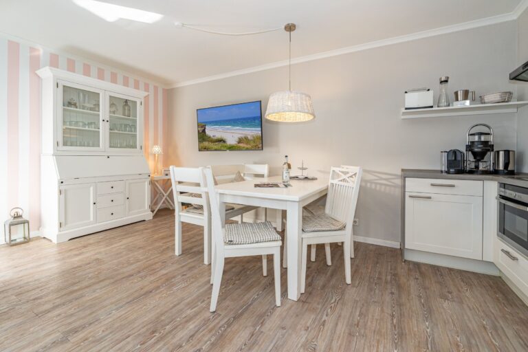 Esszimmer mit drei Stühlen und einer Bank. Links davon eine kleine Küche. Rechts davon ein Geschirrschrank