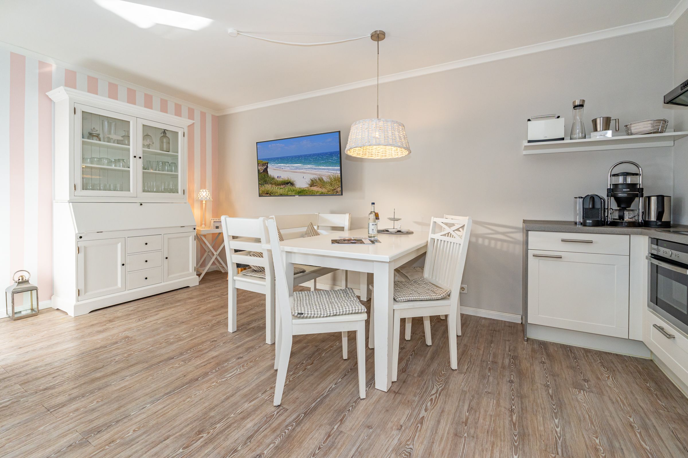 Esszimmer mit drei Stühlen und einer Bank. Links davon eine kleine Küche. Rechts davon ein Geschirrschrank