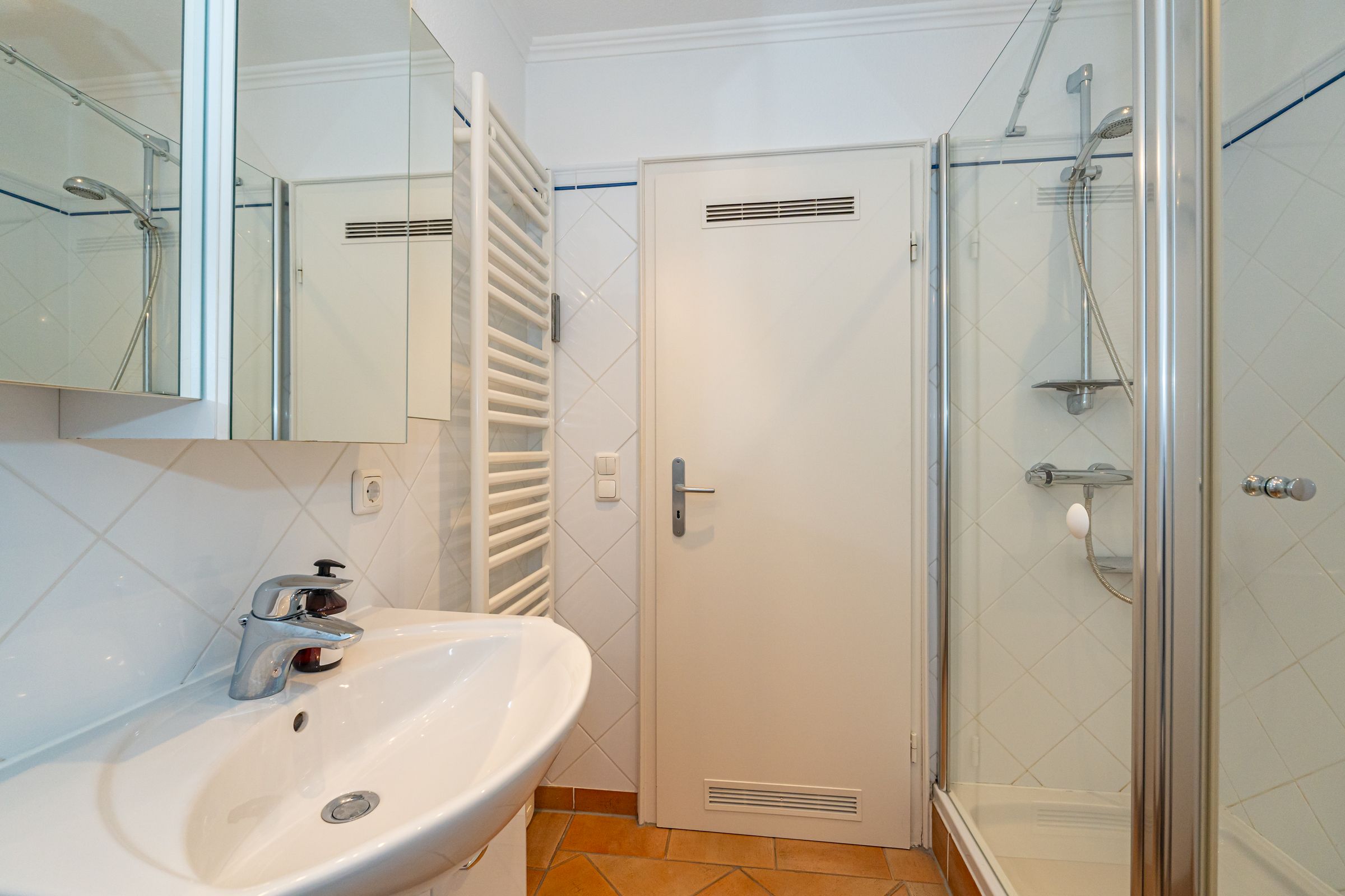 Badezimmer mit Dusche, Waschbecken und Spiegel. DAs Badezimmer hat weiße Fliesen.