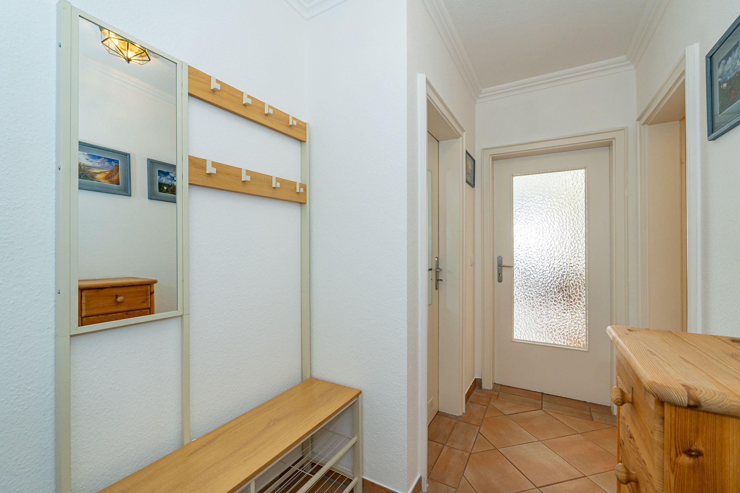 Flur mit Ankleidebank, kleinem Schrank und geschlossener Tür mit Lichtausschnitt