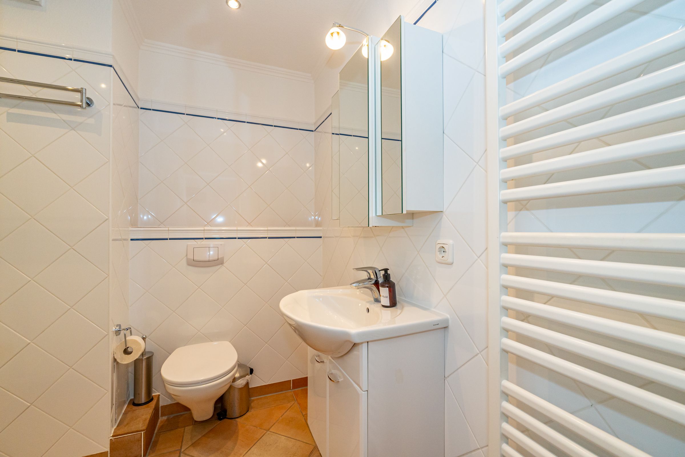 weißgefließtes Badezimmer mit Waschbecken, WC und Badspiegelschrank