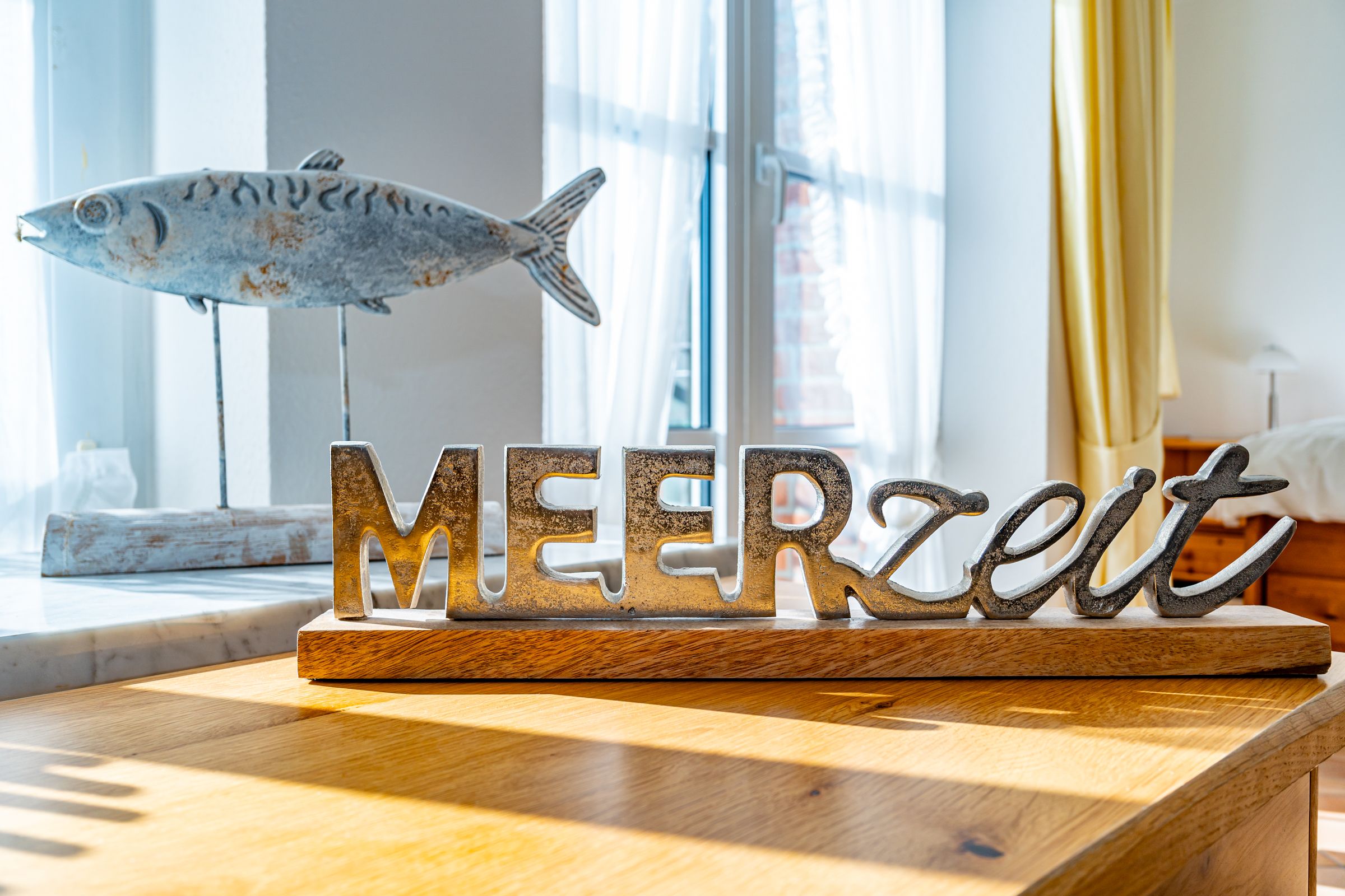 Dekorationsartikel aus Metall mit der Schrift Meerzeit. Im Hintergrund eine Fischskulptur