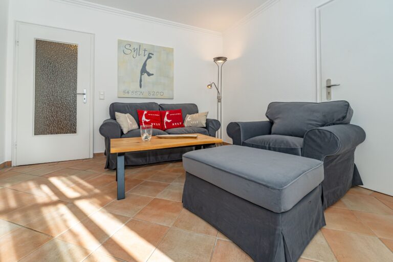 Wohnzimmergruppe mit Sofa, Sessel, Hocker und Couchtisch. An der Wand ein Bild mit Sylt-Karte.