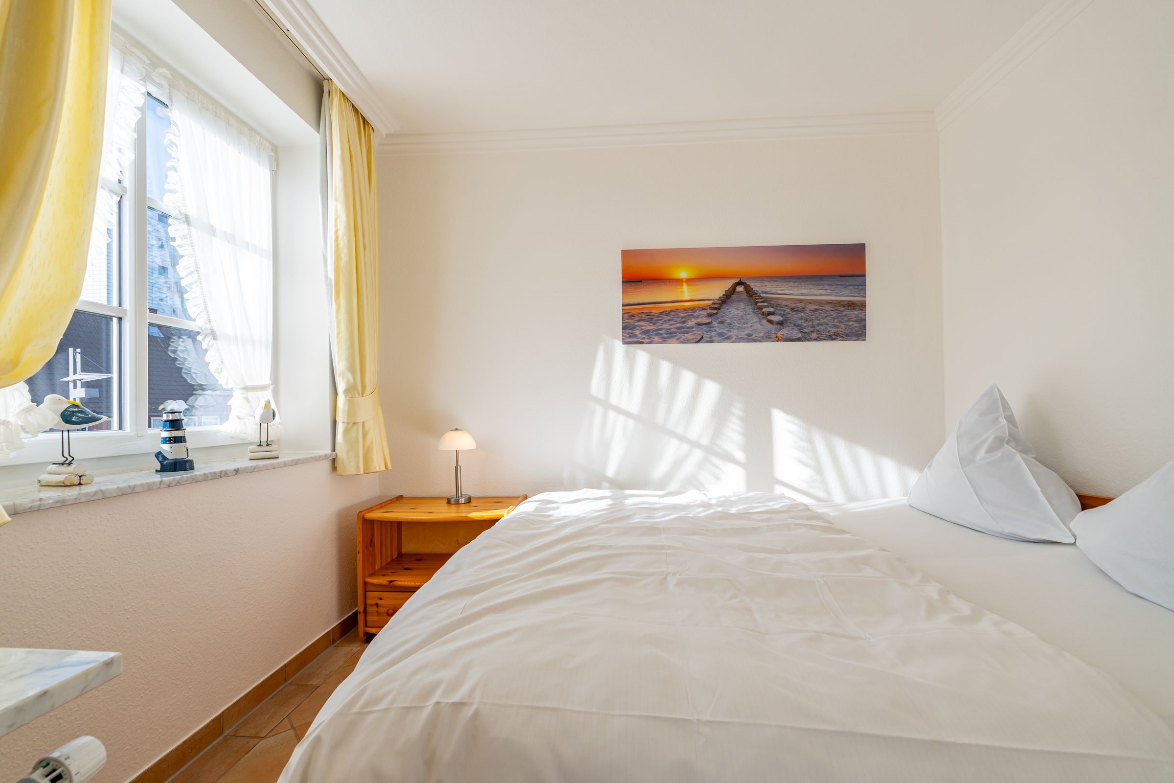 Schlafzimmer mit Doppelbett und Fenster. An der Wand hängt ein Bild mit Strandmotiv