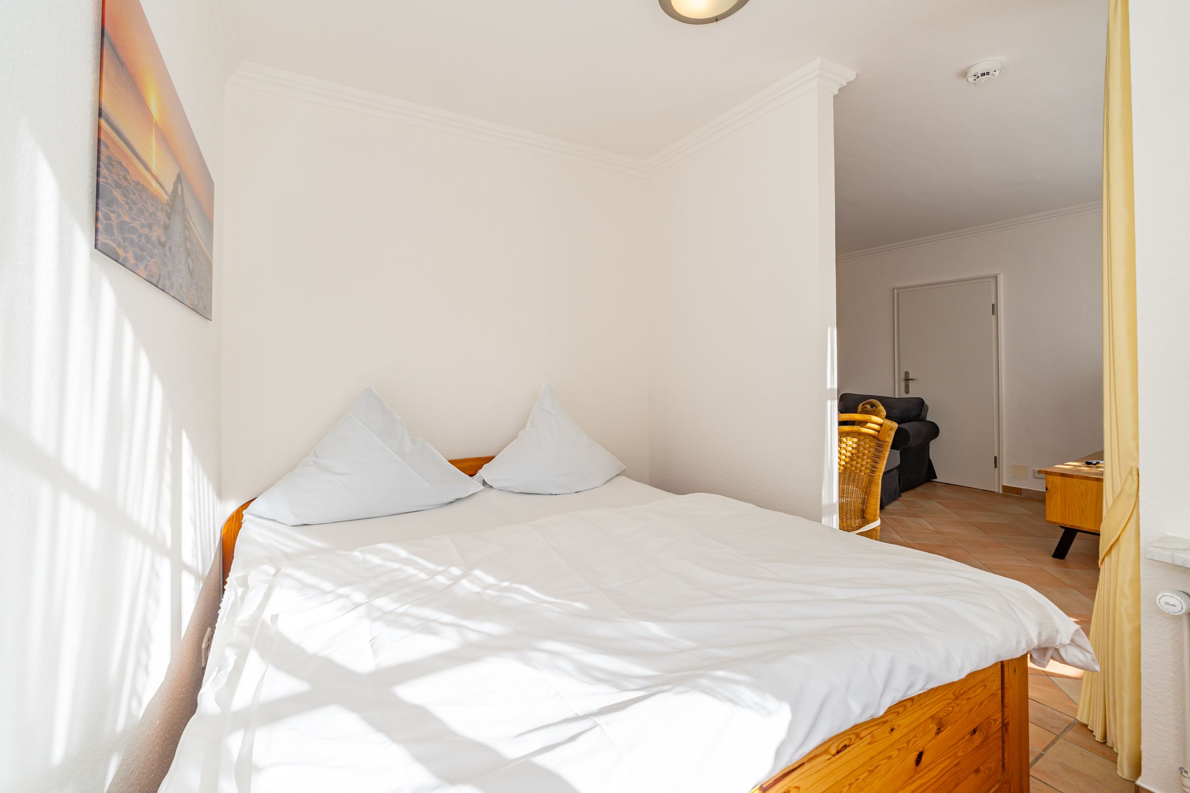 Schlafzimmer mit Doppelbett aus Holz und Blick in den Wohnbereich.