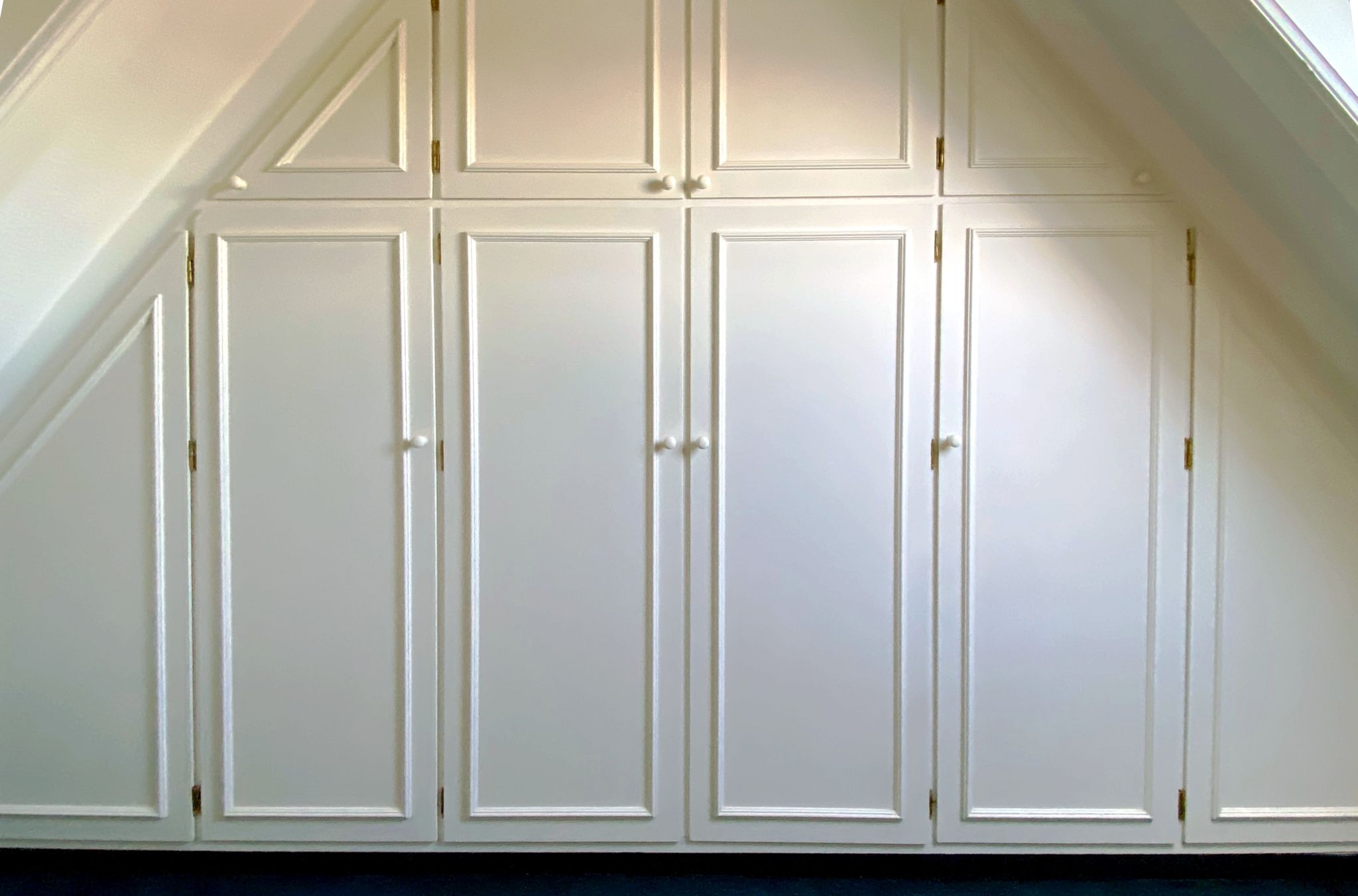 Ein Schrank in eine Wand eingebaut. Die Wand hat auf beiden SEiten eine Dachschräge. Der Schrank besteht aus 4 Türen mit gleicehr Größe und zwei kleineren Türen