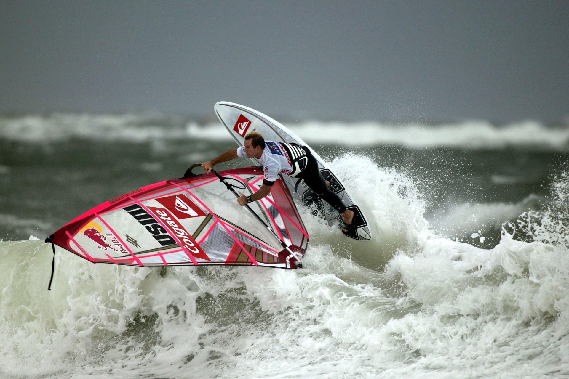 Ein Windsurfer reitet eine Welle auf dem Meer. Mit dem Segel fängt er kunstvoll den Wind auf der Welle ein.