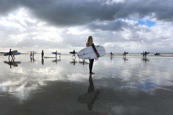 Mehrere Surfer mit Surfboard unter dem Arm am Strand
